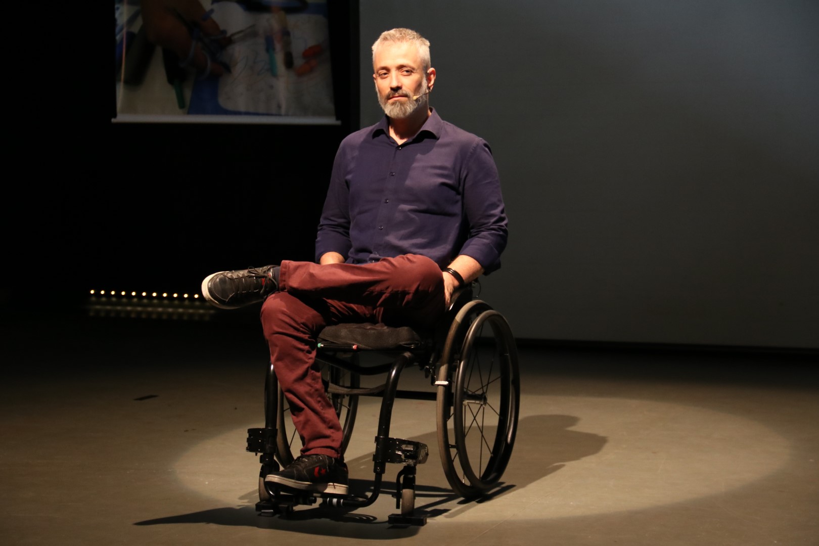 no palco, o ator Luciano Mallmann, que usa uma cadeira de rodas. Um luz bem de leve está sobre ele.